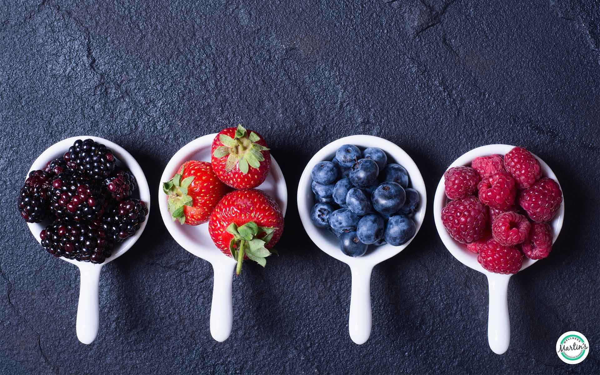 Blackberries, strawberries, blueberries, and raspberries in white cups on dark background – antioxidant-rich berries for brain, heart, and immune health