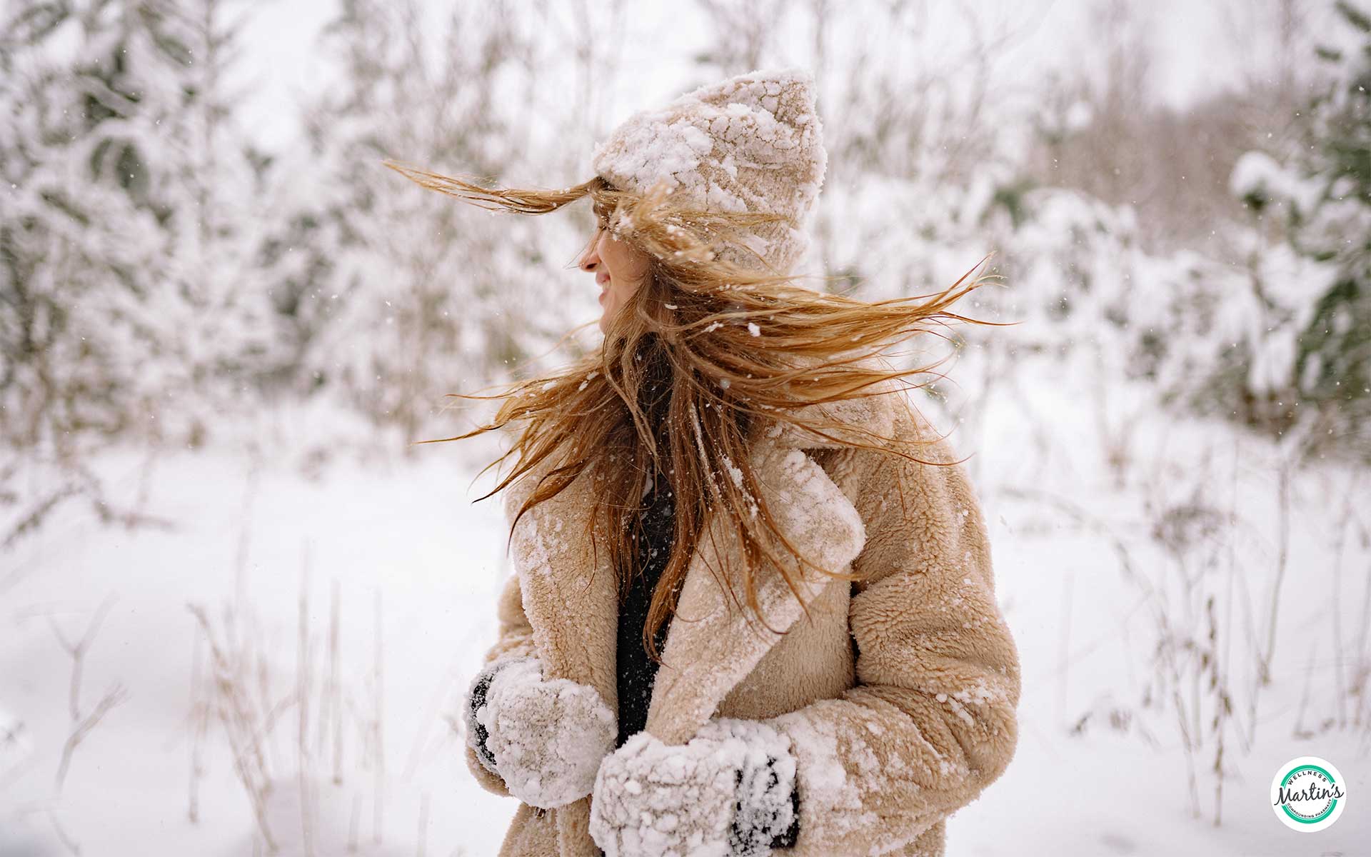 A person in a tan coat and beanie stands in a snowy landscape