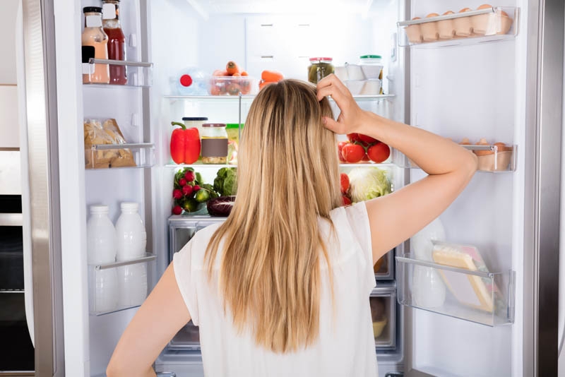 woman contemplating in front of a refrigerator- wondering if she should refrigerate her probiotics.