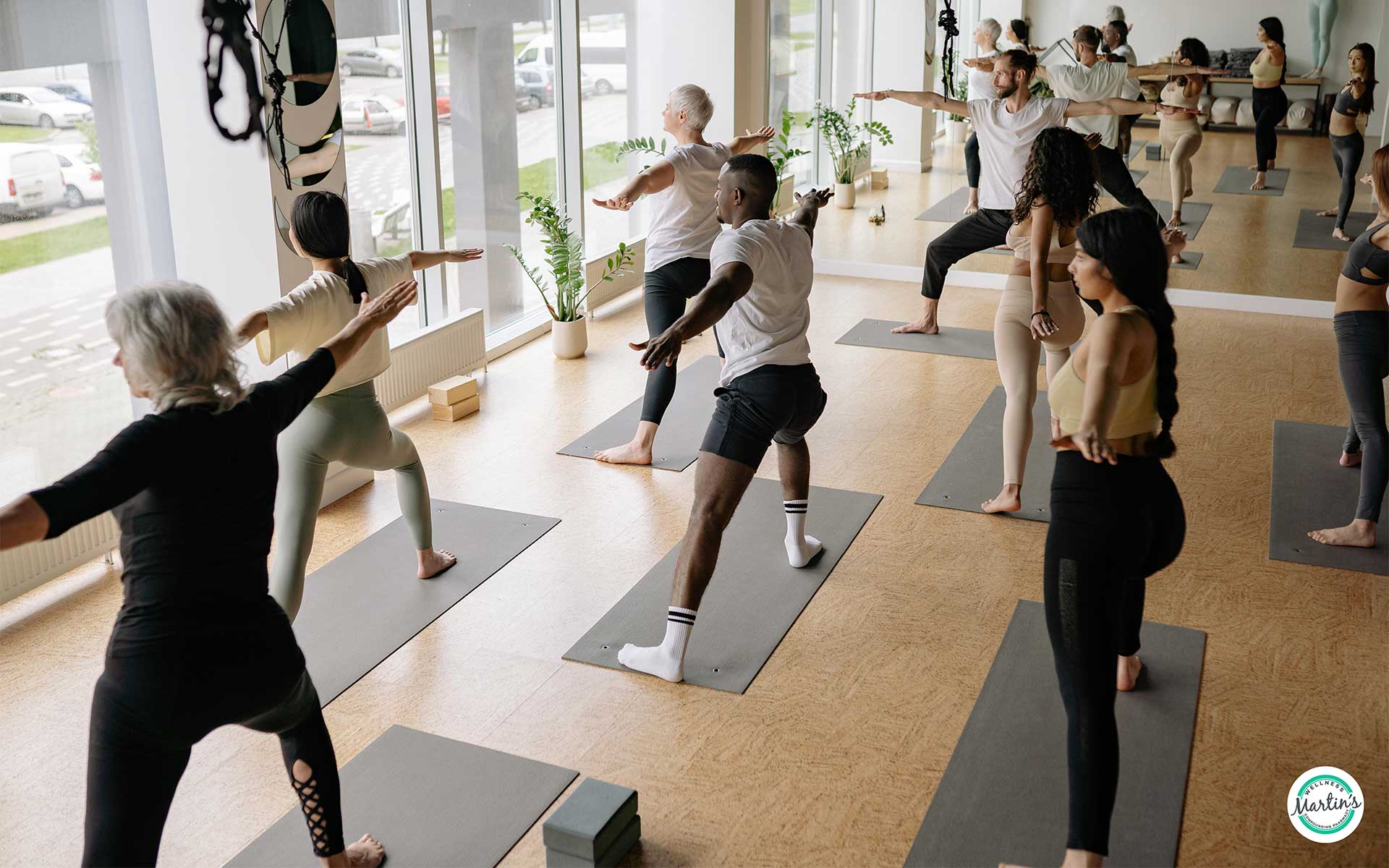 A group of people practicing yoga poses on mats in a bright studio with large windows and mirrored walls