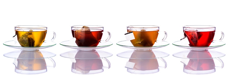 Four glasses of tea in a row, each with their own tea bag and unique coloring