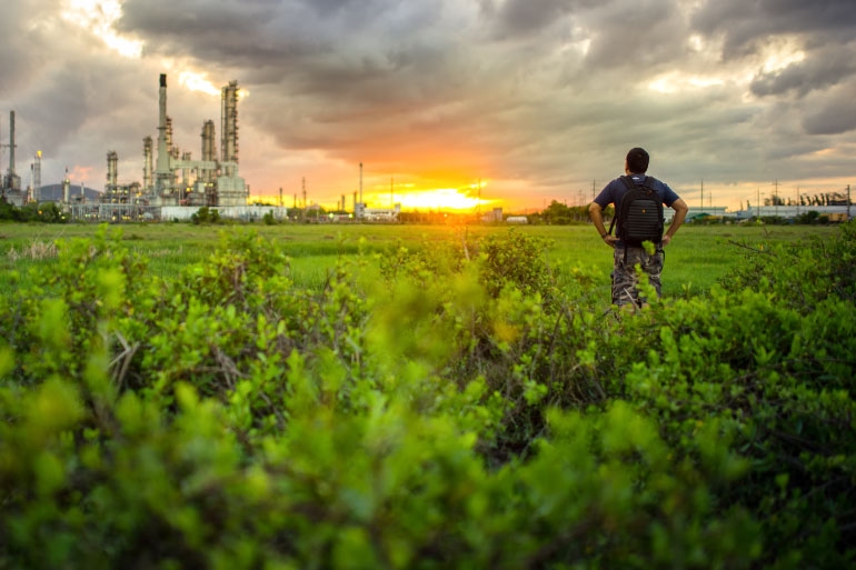 Man standing in front of a factory, releasing toxic metals into the air and soil